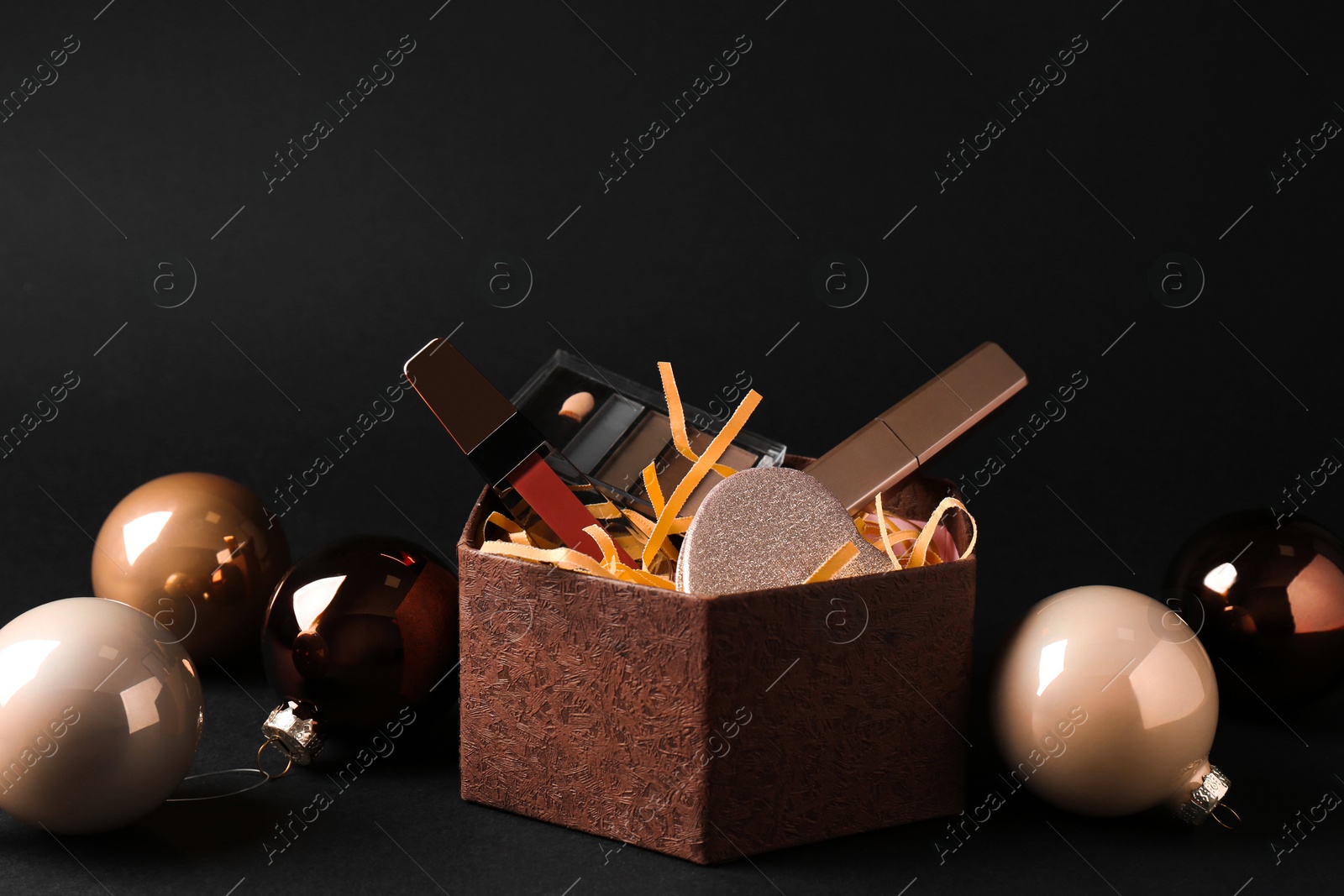 Photo of Gift box with decorative cosmetics and Christmas balls on black background. Space for text