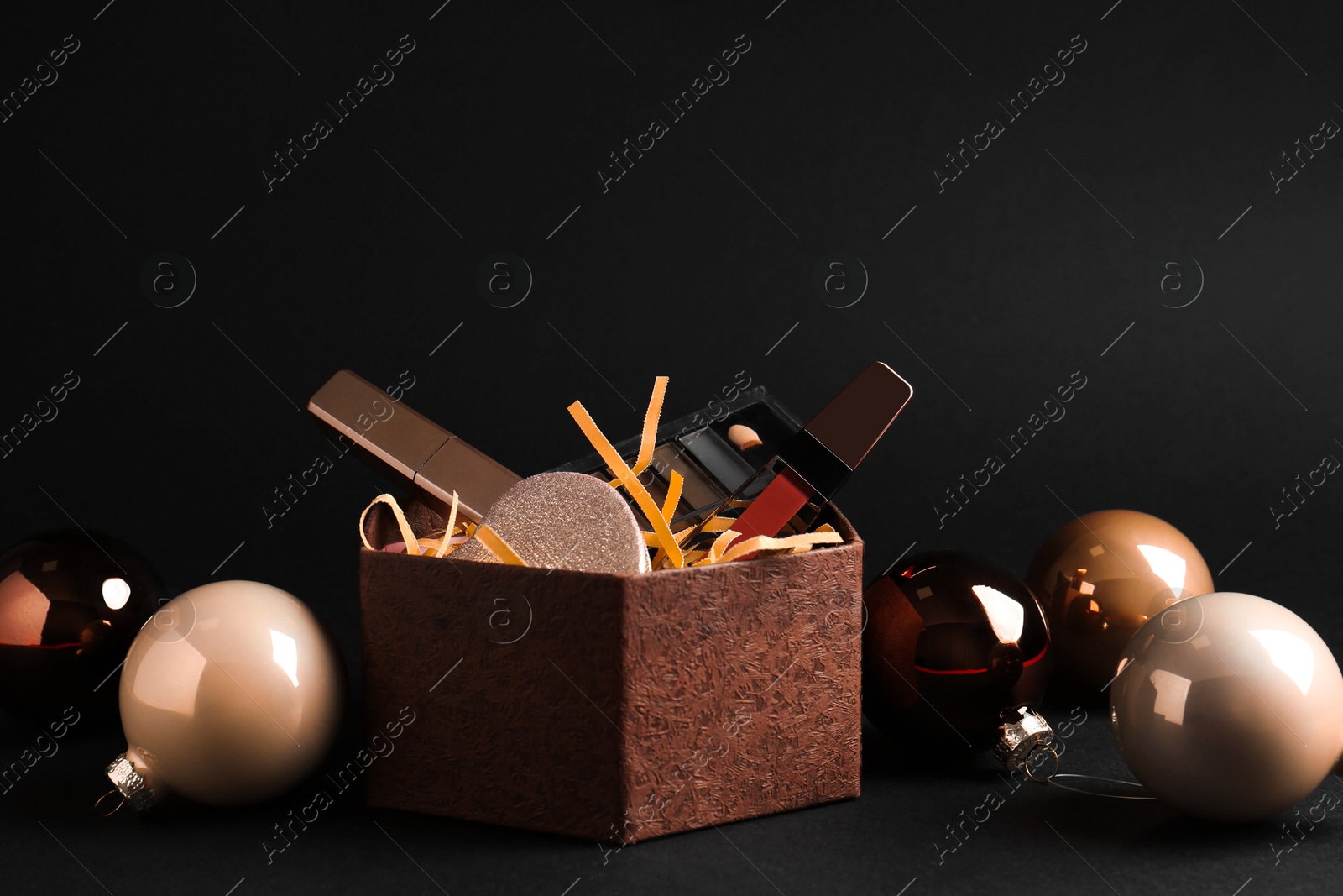 Photo of Gift box with decorative cosmetics and Christmas balls on black background. Space for text