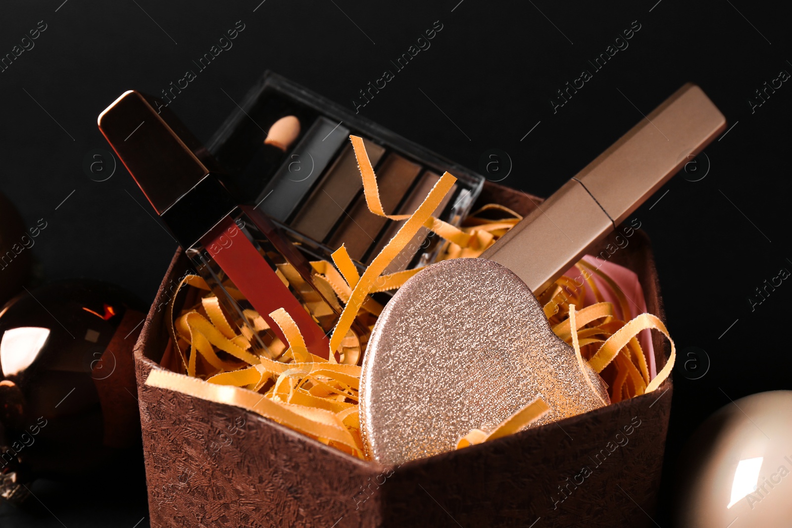 Photo of Gift box with decorative cosmetics and Christmas balls on black background, closeup