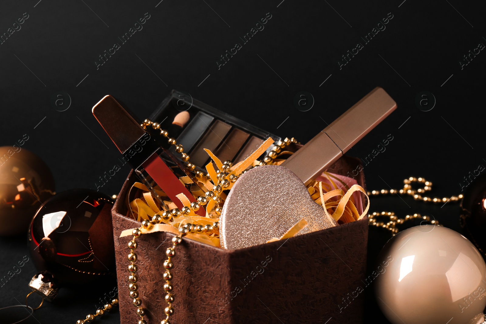 Photo of Gift box with decorative cosmetics and Christmas balls on black background, closeup