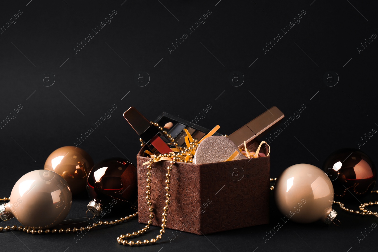 Photo of Gift box with decorative cosmetics and Christmas balls on black background. Space for text