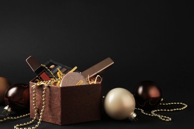 Gift box with decorative cosmetics and Christmas balls on black background. Space for text