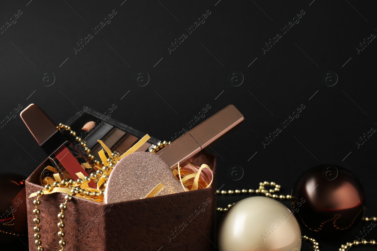 Photo of Gift box with decorative cosmetics and Christmas balls on black background. Space for text