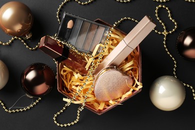 Photo of Gift box with decorative cosmetics and Christmas balls on black background, flat lay