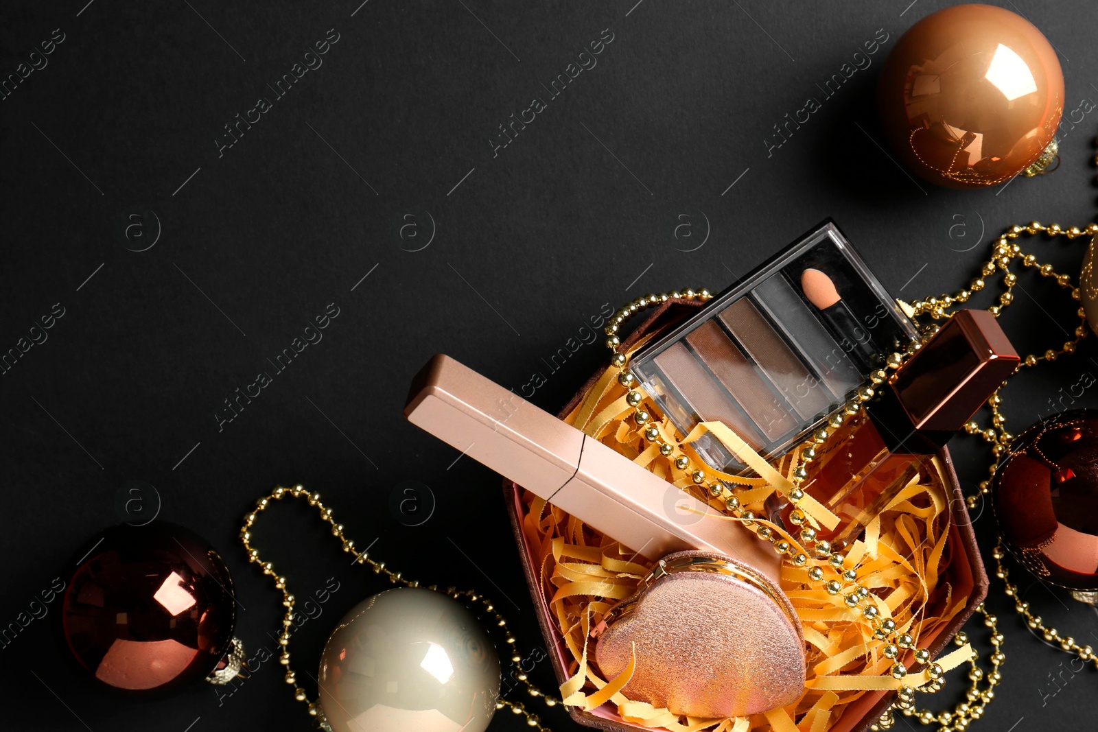 Photo of Gift box with decorative cosmetics and Christmas balls on black background, flat lay. Space for text