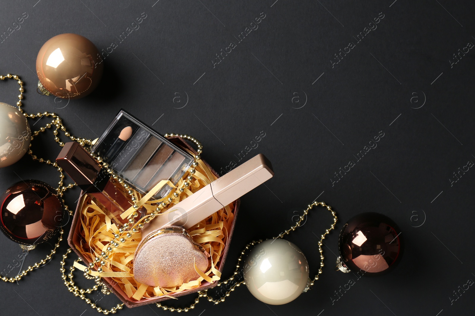 Photo of Gift box with decorative cosmetics and Christmas balls on black background, flat lay. Space for text