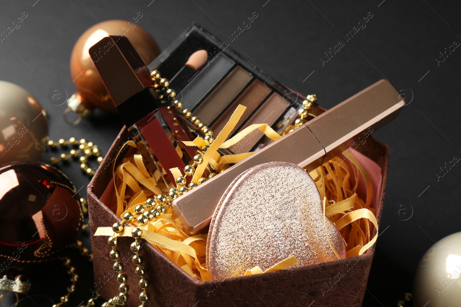 Photo of Gift box with decorative cosmetics and Christmas balls on black background, closeup