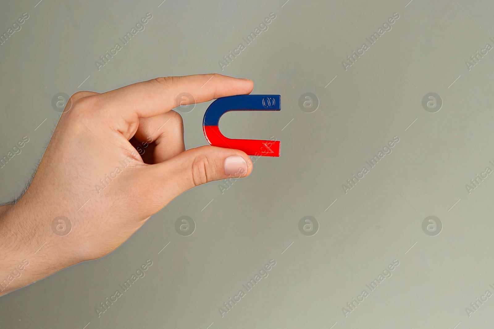 Photo of Man holding horseshoe magnet on grey background, closeup. Space for text