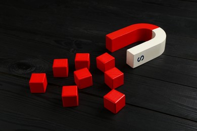 Photo of Magnet attracting red cubes on black wooden table