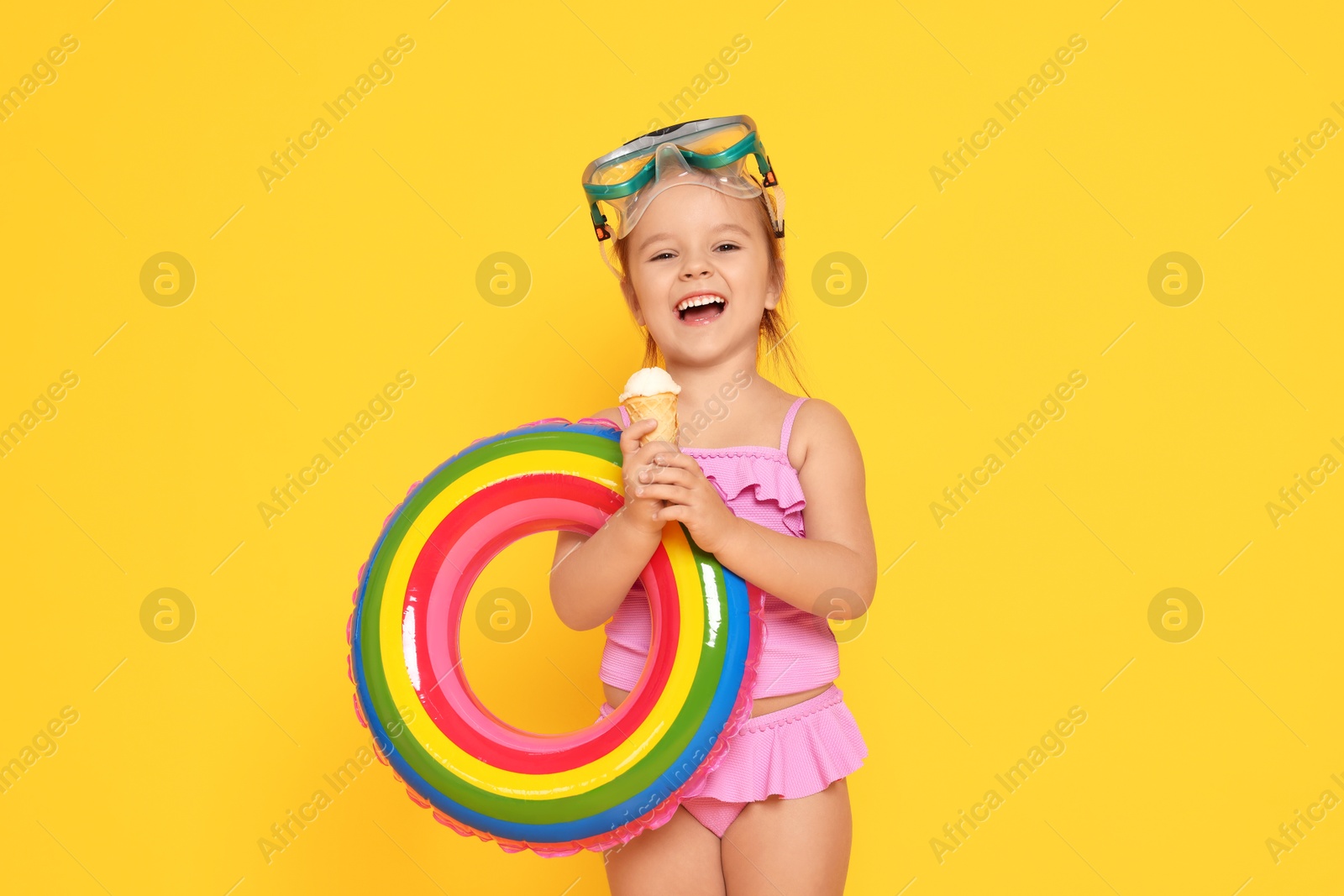 Photo of Cute little girl in swimsuit with inflatable ring eating ice cream on orange background