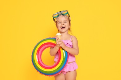 Photo of Cute little girl in swimsuit with inflatable ring eating ice cream on orange background