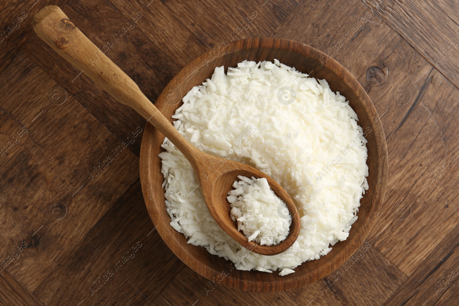 Photo of White soy wax flakes in bowl and spoon on wooden table, top view