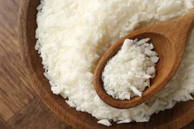 Photo of White soy wax flakes in bowl and spoon on wooden table, top view