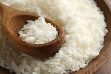 Photo of White soy wax flakes in bowl and spoon on wooden table, closeup