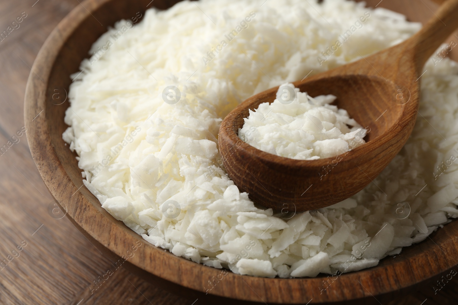 Photo of White soy wax flakes in bowl and spoon on wooden table, closeup