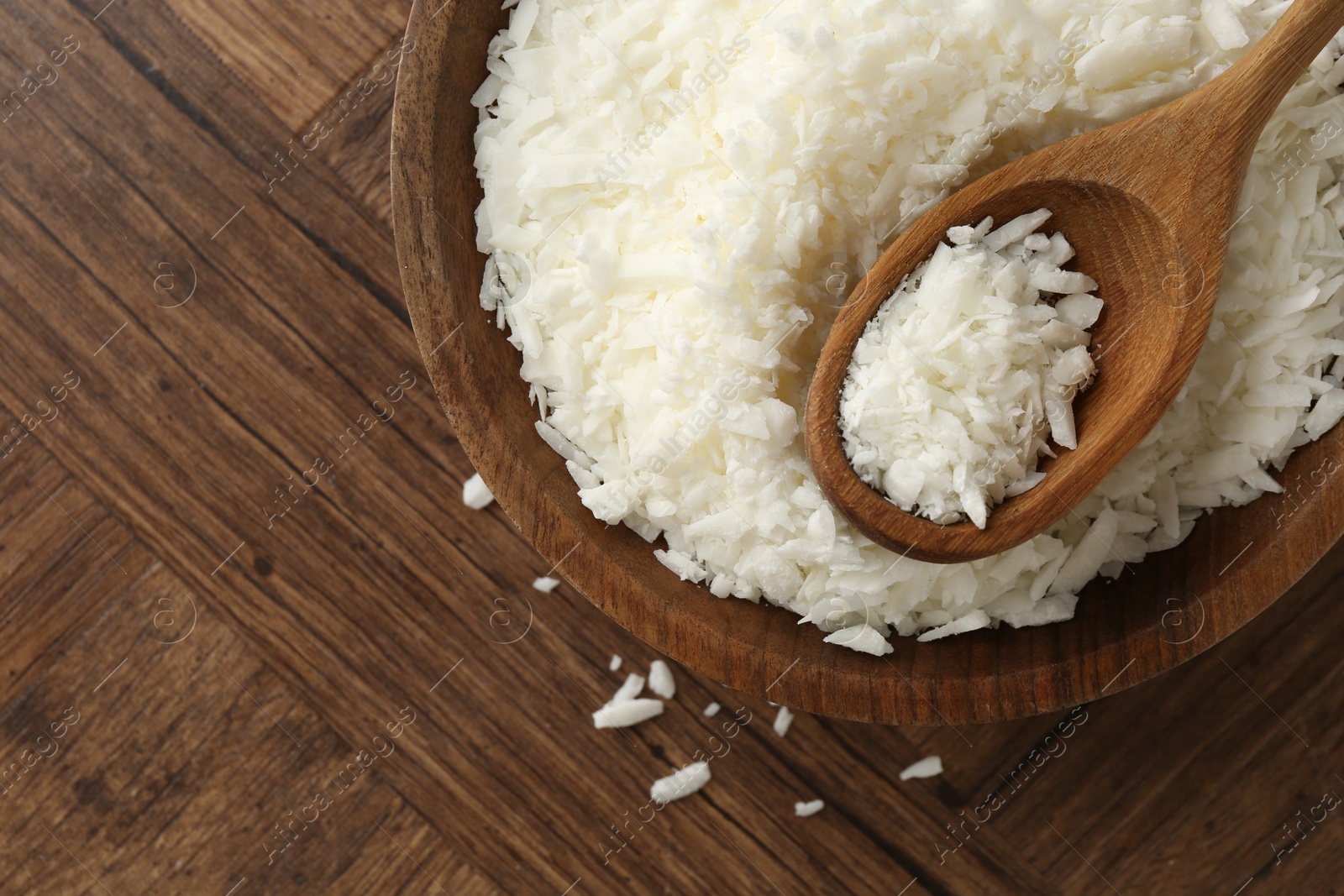 Photo of White soy wax flakes in bowl and spoon on wooden table, top view