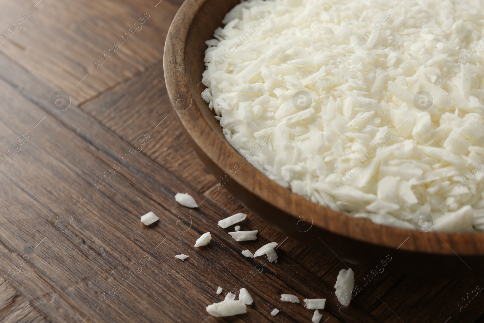 Photo of White soy wax flakes in bowl on wooden table, closeup