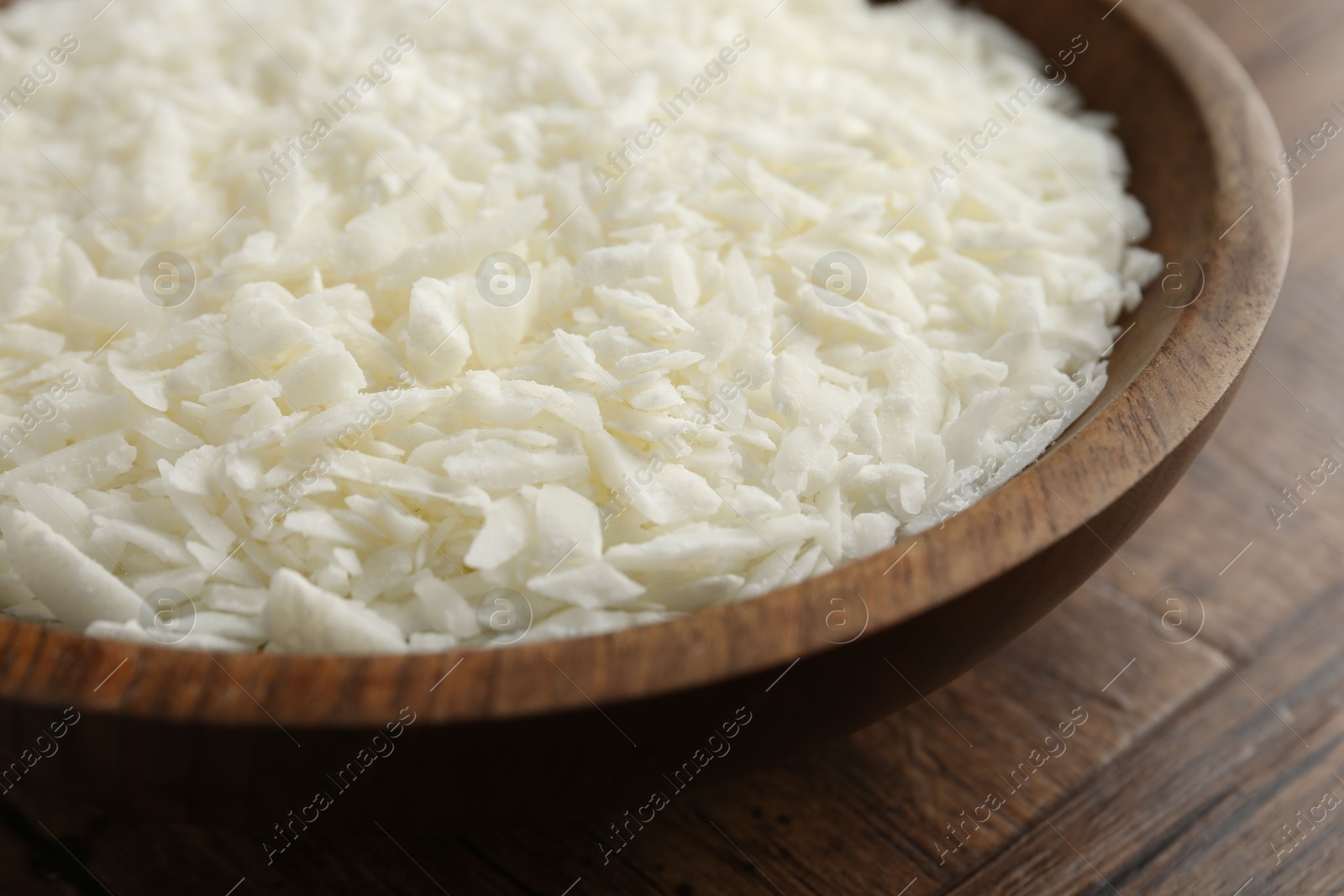 Photo of White soy wax flakes in bowl on wooden table, closeup