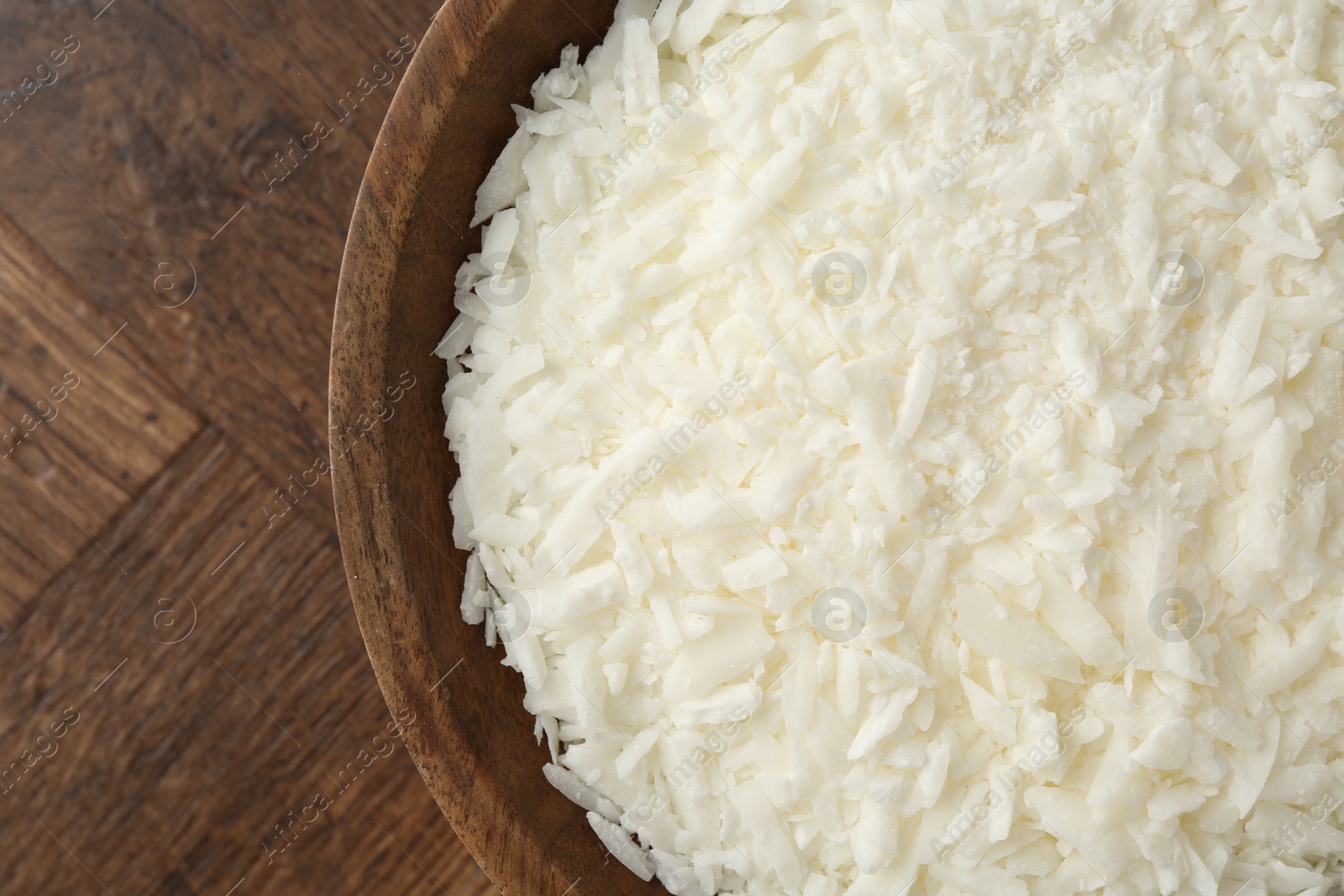 Photo of White soy wax flakes in bowl on wooden table, closeup