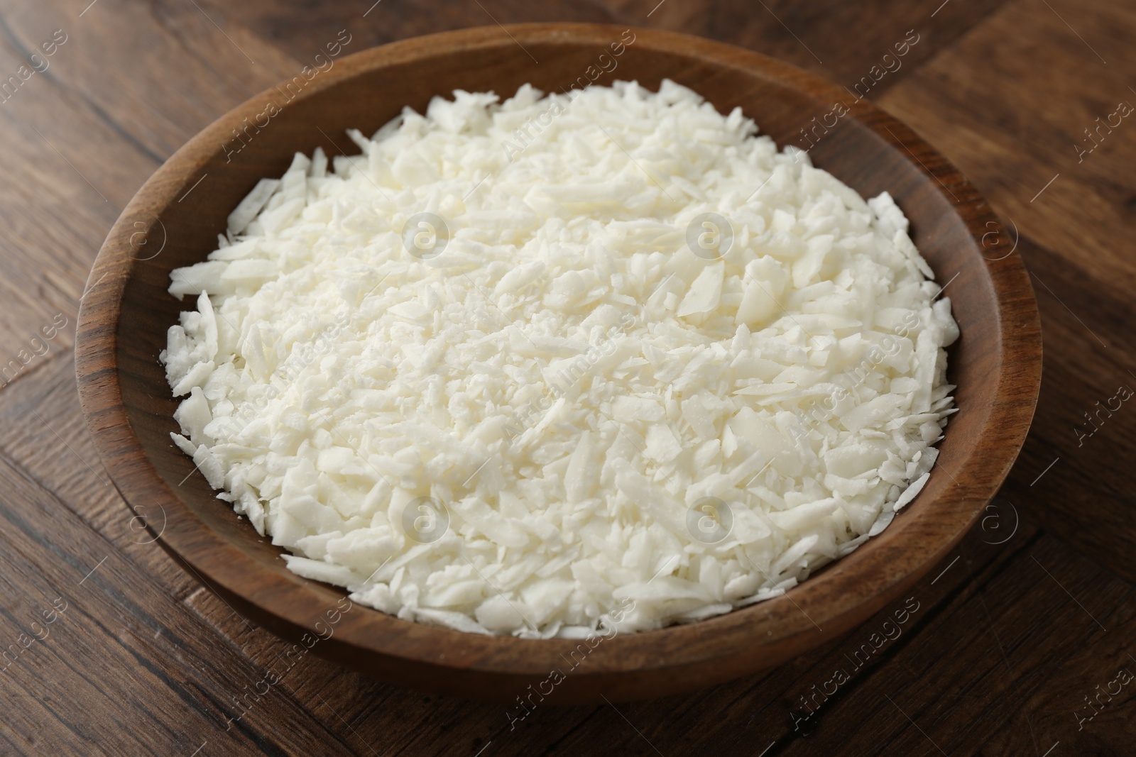 Photo of White soy wax flakes in bowl on wooden table, closeup