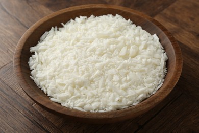 Photo of White soy wax flakes in bowl on wooden table, closeup