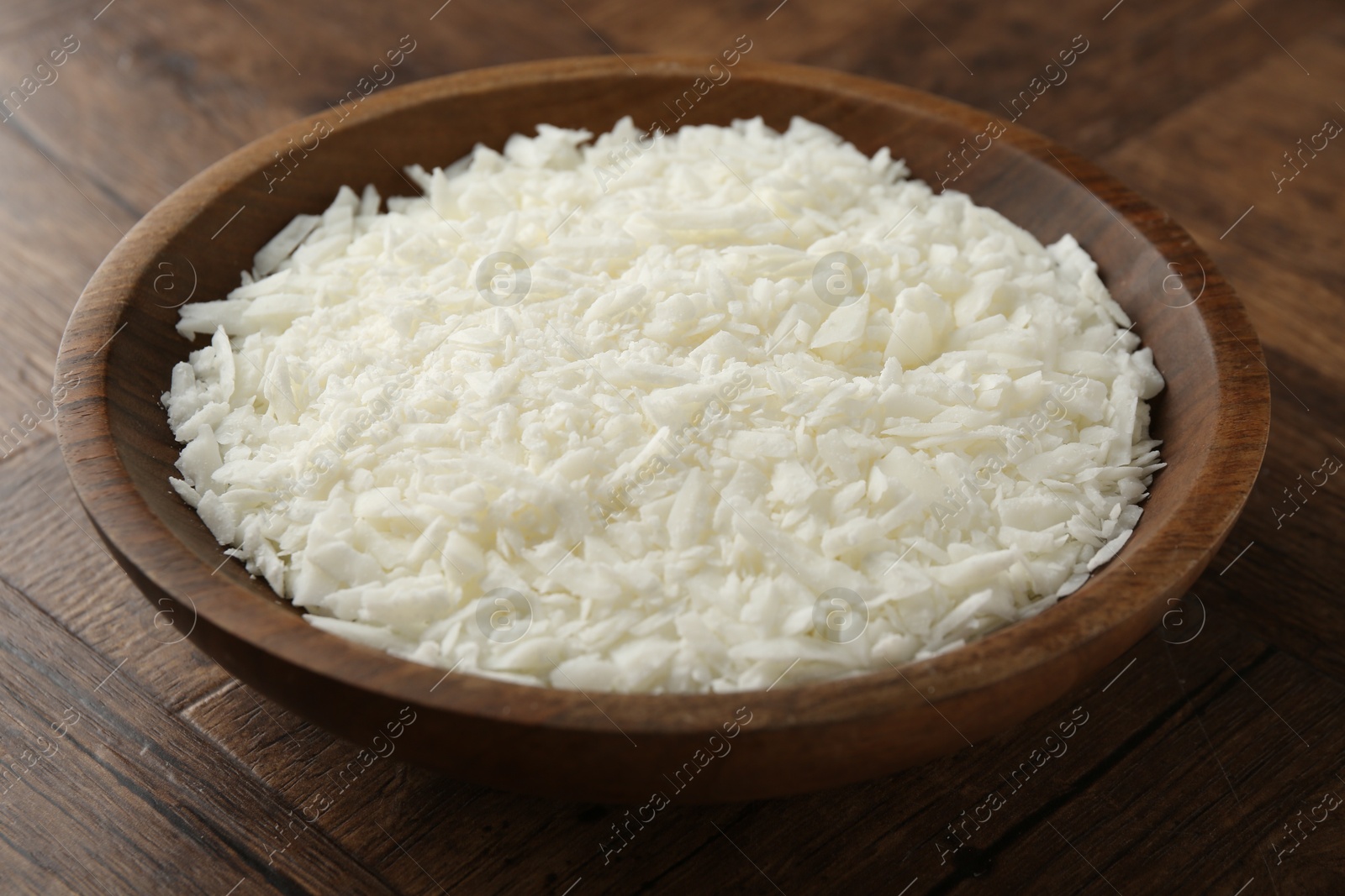 Photo of White soy wax flakes in bowl on wooden table, closeup