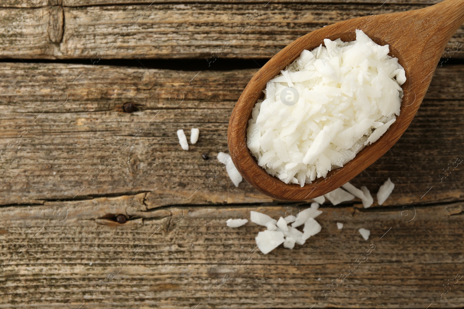 Photo of White soy wax flakes in spoon on wooden table, top view. Space for text