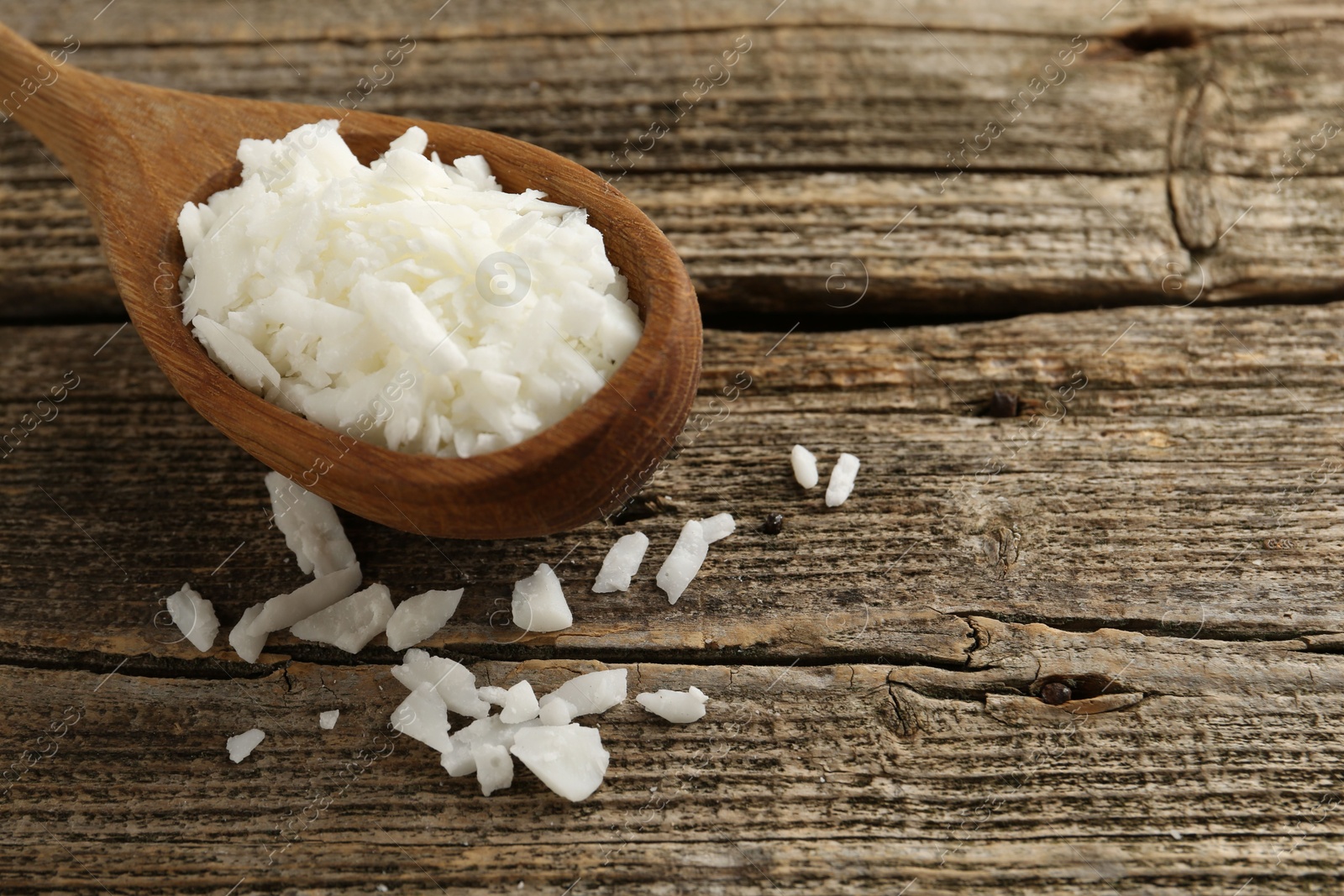 Photo of White soy wax flakes in spoon on wooden table, closeup. Space for text