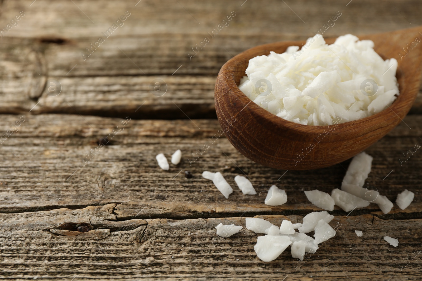 Photo of White soy wax flakes in spoon on wooden table, closeup. Space for text