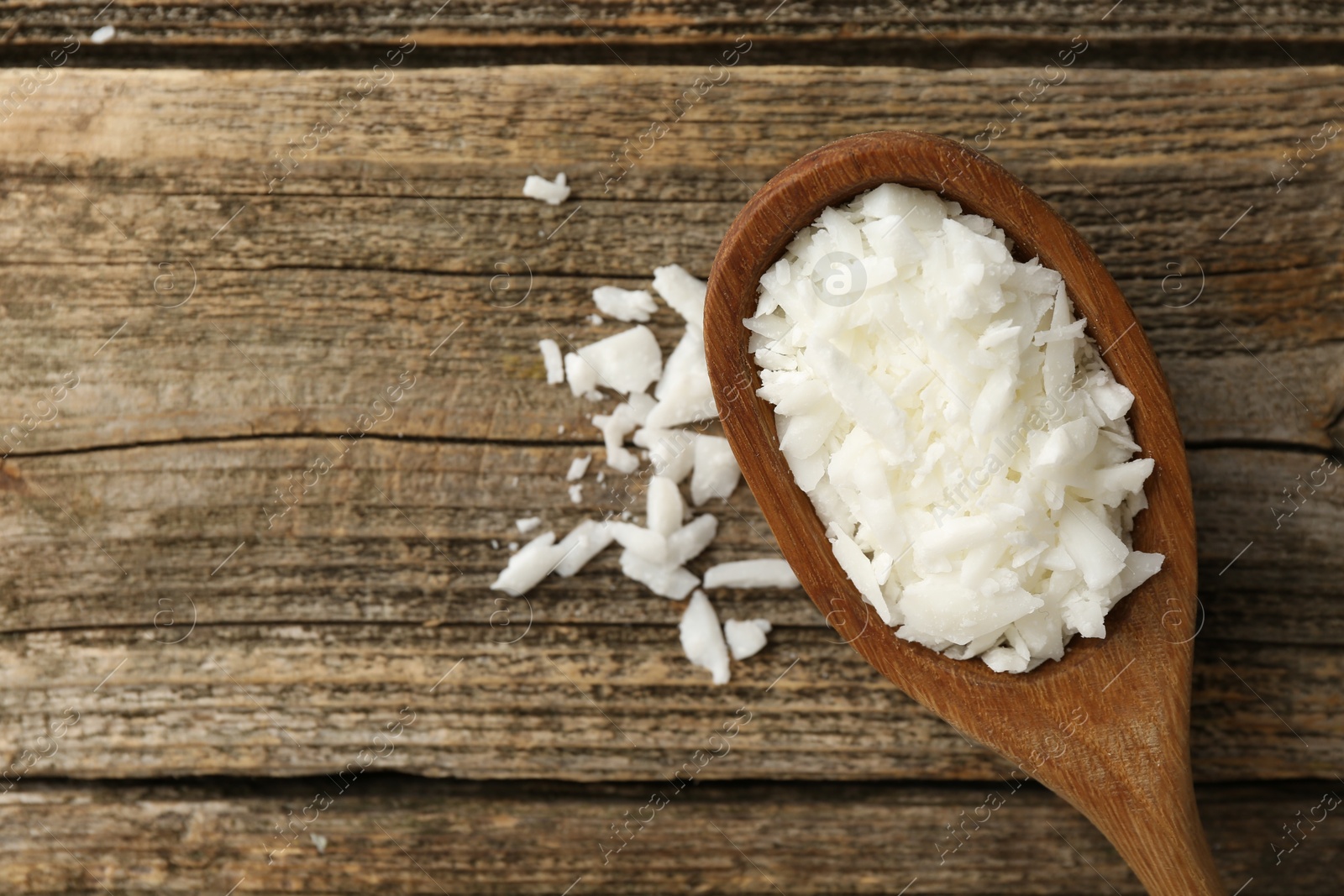 Photo of White soy wax flakes in spoon on wooden table, top view. Space for text