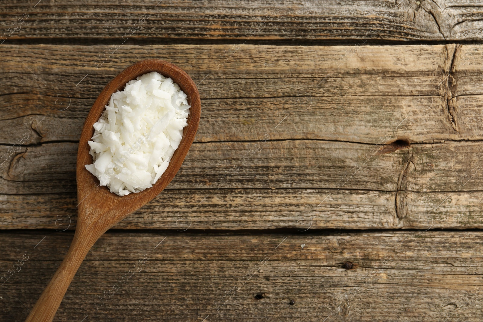 Photo of White soy wax flakes in spoon on wooden table, top view. Space for text