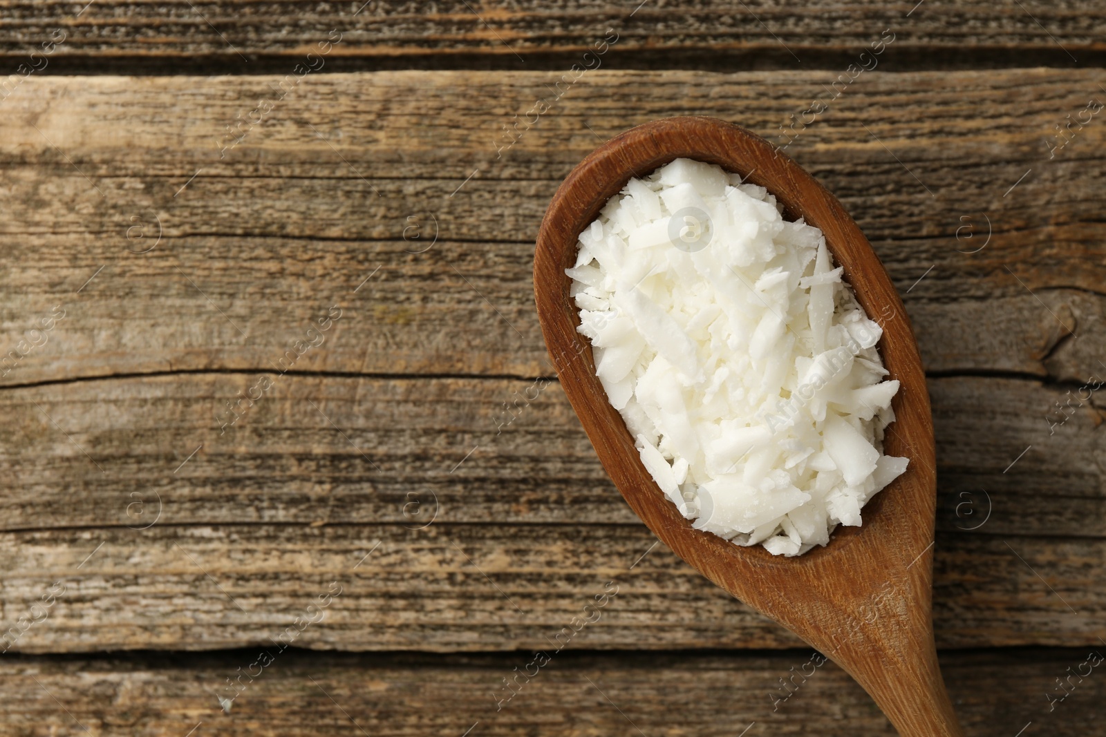 Photo of White soy wax flakes in spoon on wooden table, top view. Space for text