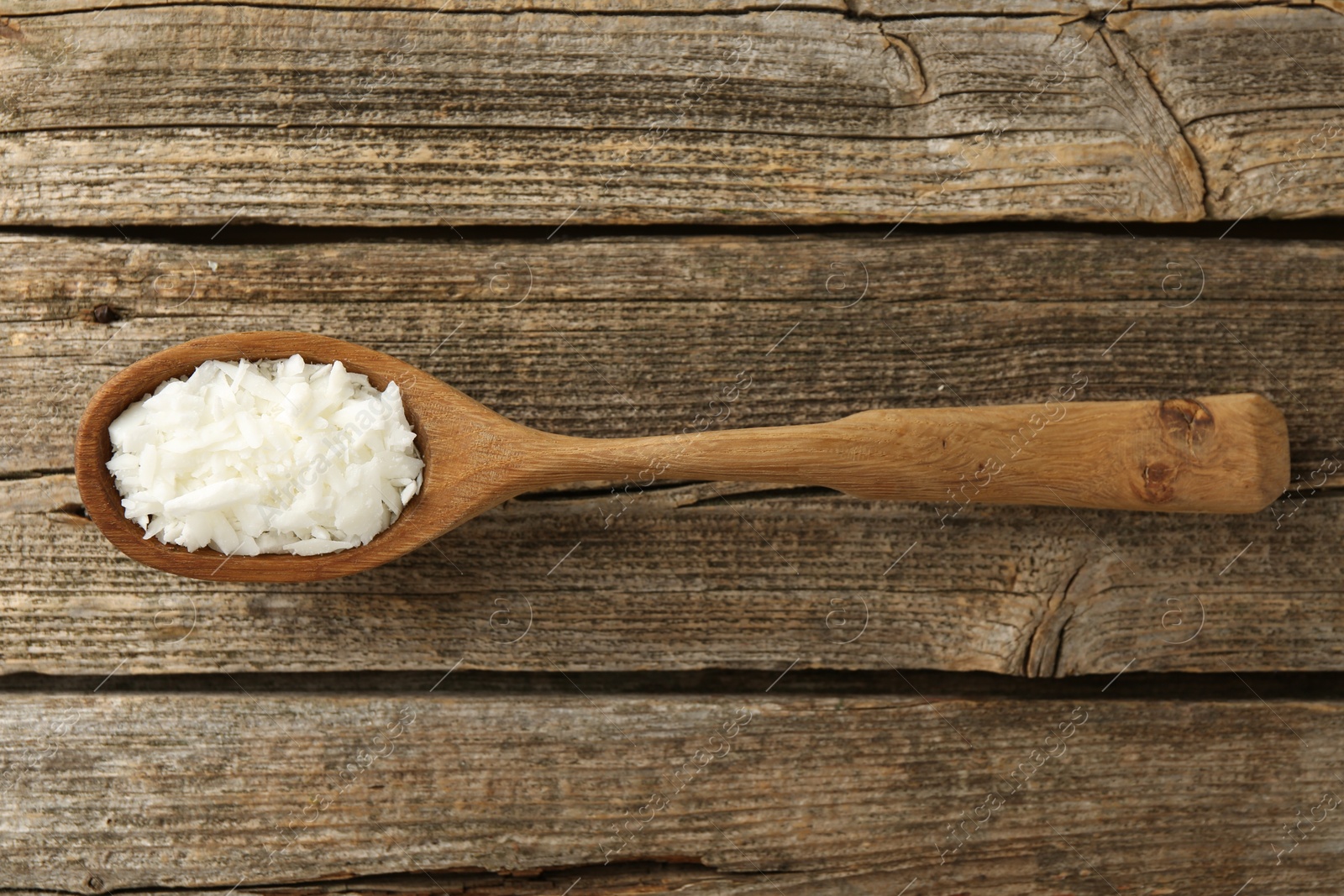 Photo of White soy wax flakes in spoon on wooden table, top view