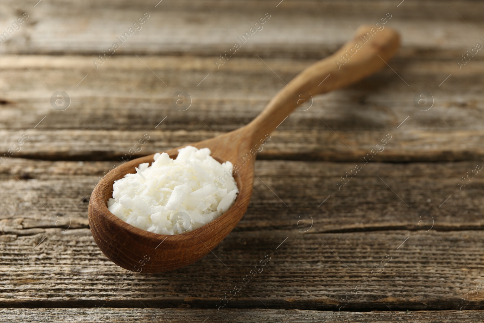 Photo of White soy wax flakes in spoon on wooden table, closeup