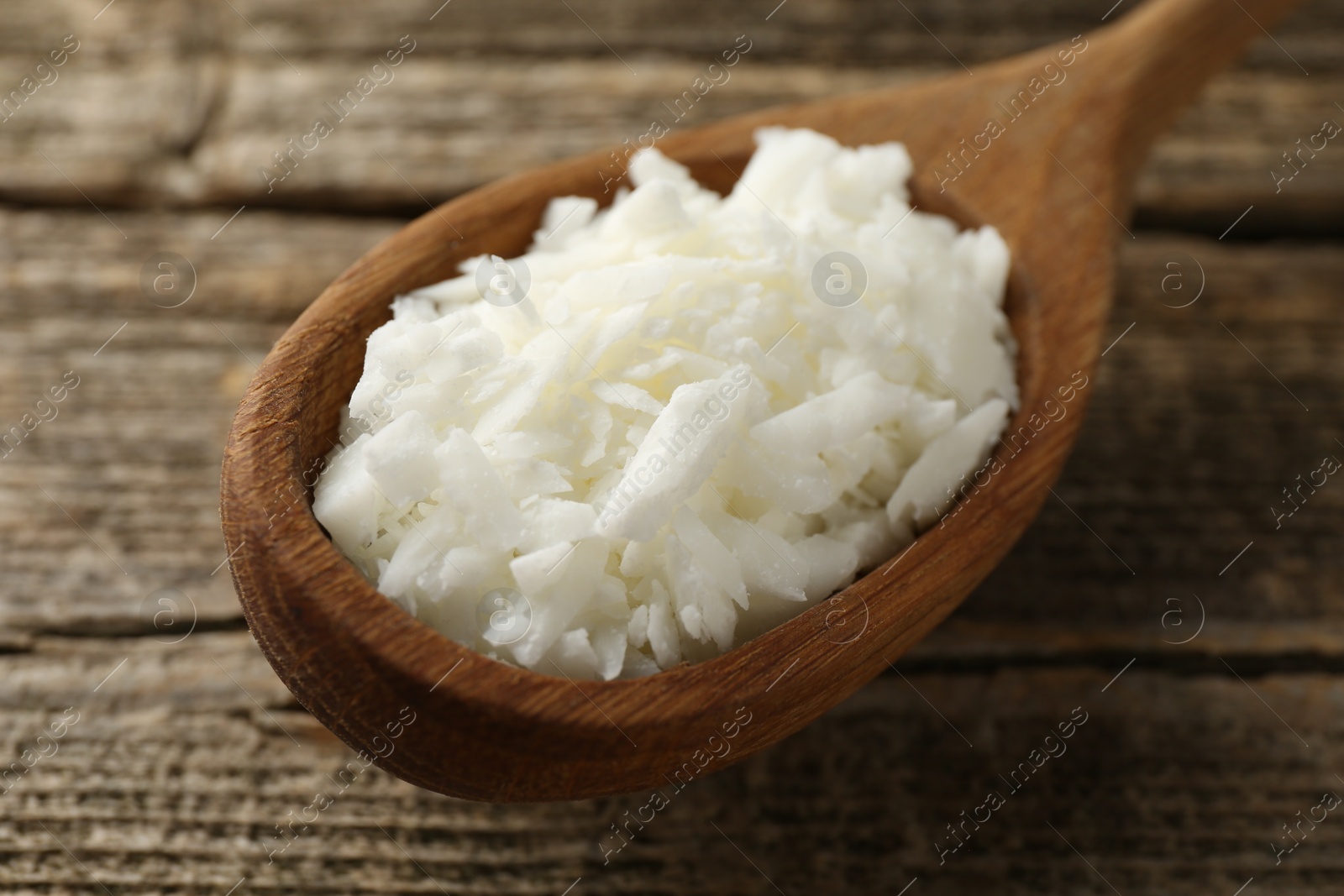 Photo of White soy wax flakes in spoon on wooden table, closeup