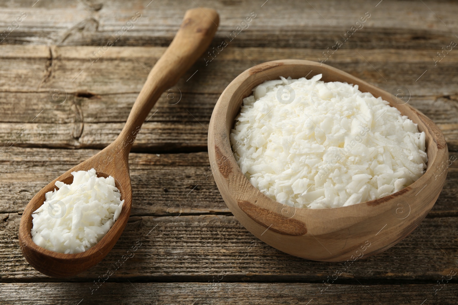 Photo of White soy wax flakes in bowl and spoon on wooden table, closeup