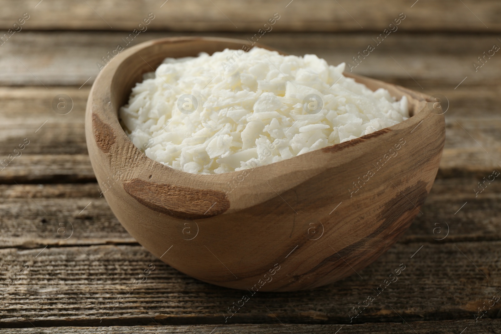 Photo of White soy wax flakes in bowl on wooden table, closeup