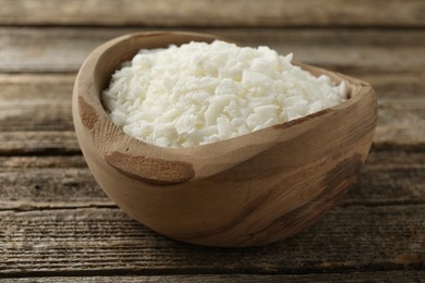 Photo of White soy wax flakes in bowl on wooden table, closeup