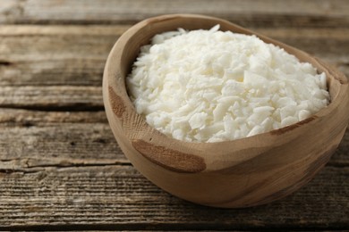 White soy wax flakes in bowl on wooden table, closeup