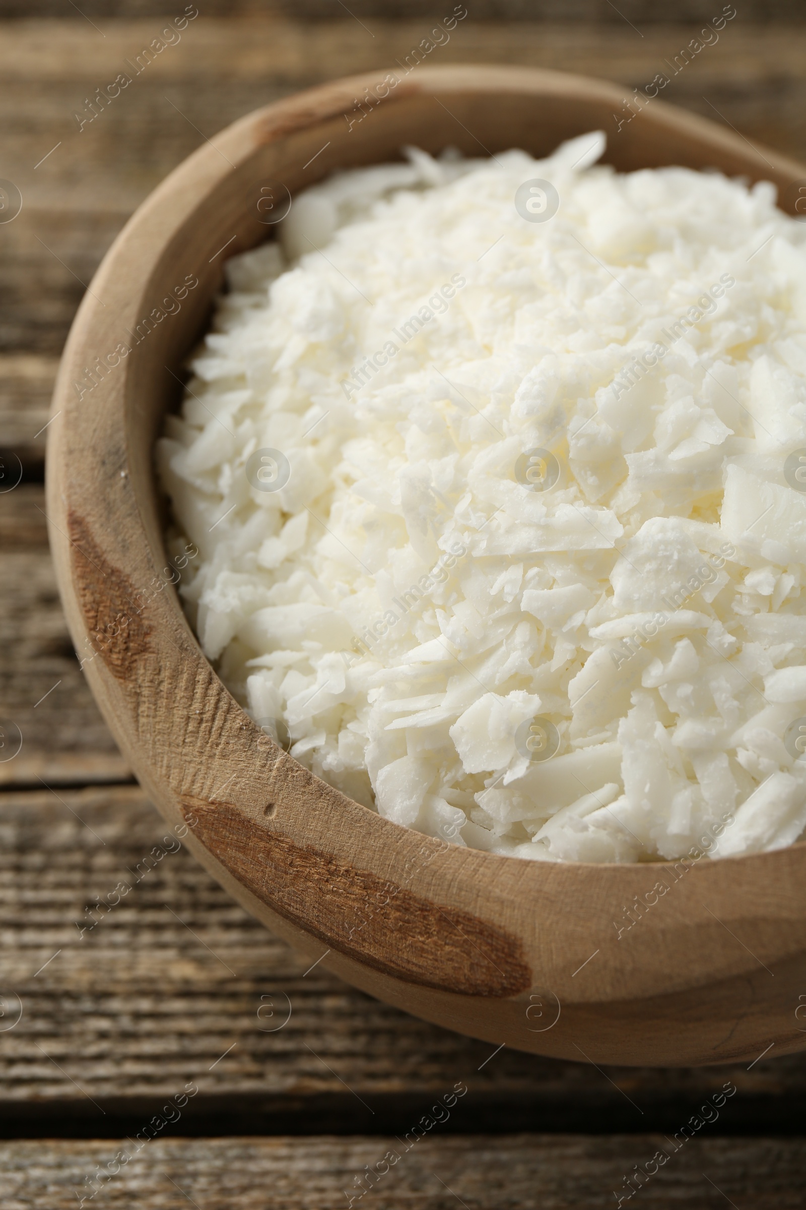 Photo of White soy wax flakes in bowl on wooden table, closeup