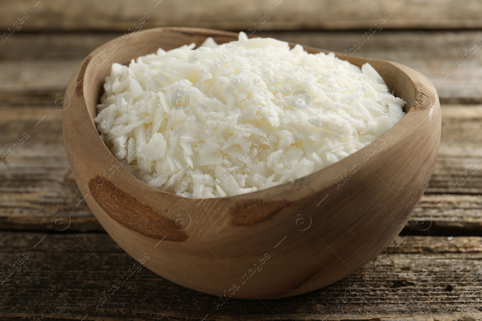 Photo of White soy wax flakes in bowl on wooden table, closeup