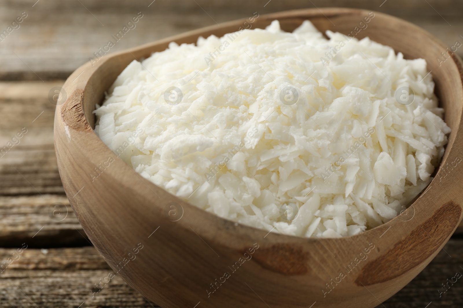 Photo of White soy wax flakes in bowl on wooden table, closeup