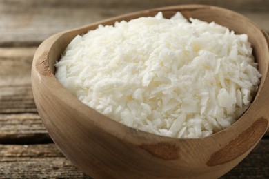 Photo of White soy wax flakes in bowl on wooden table, closeup