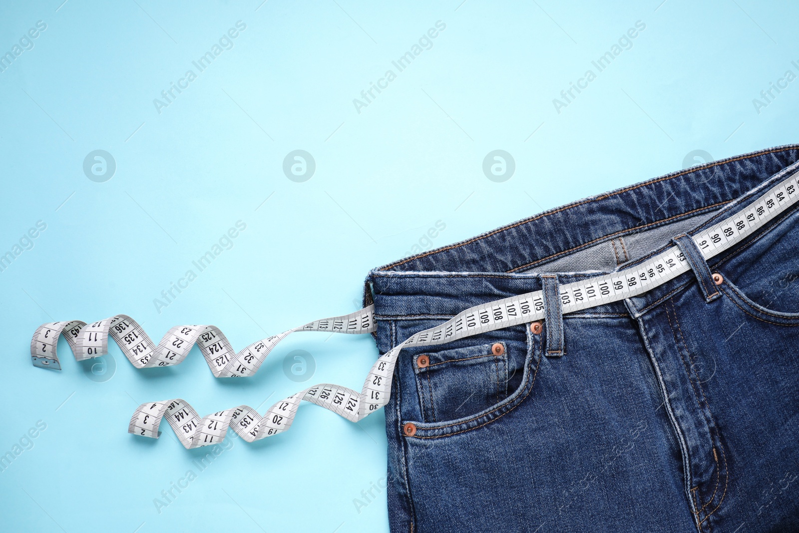 Photo of Jeans and measuring tape on light blue background, top view. Space for text