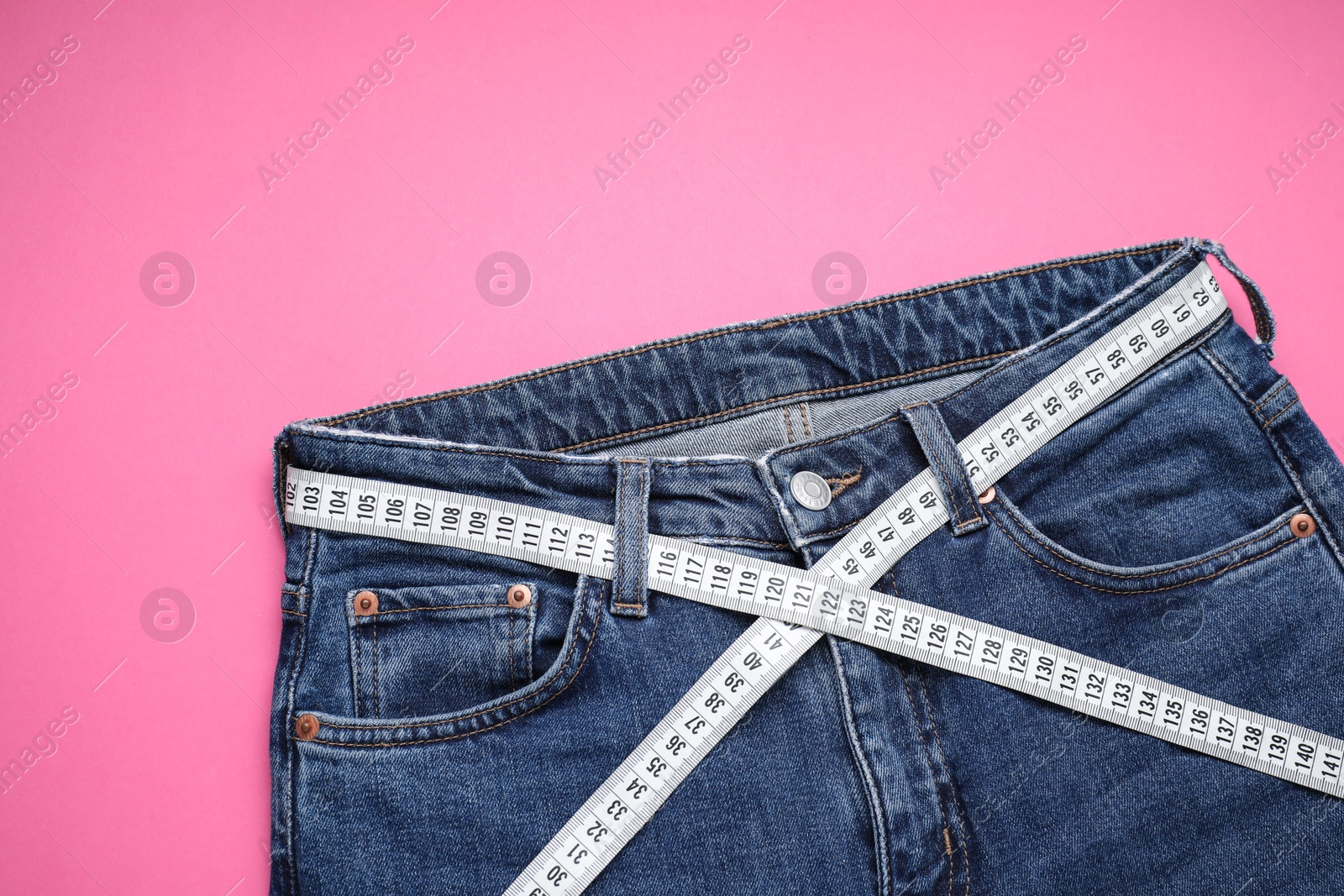 Photo of Jeans and measuring tape on pink background, top view