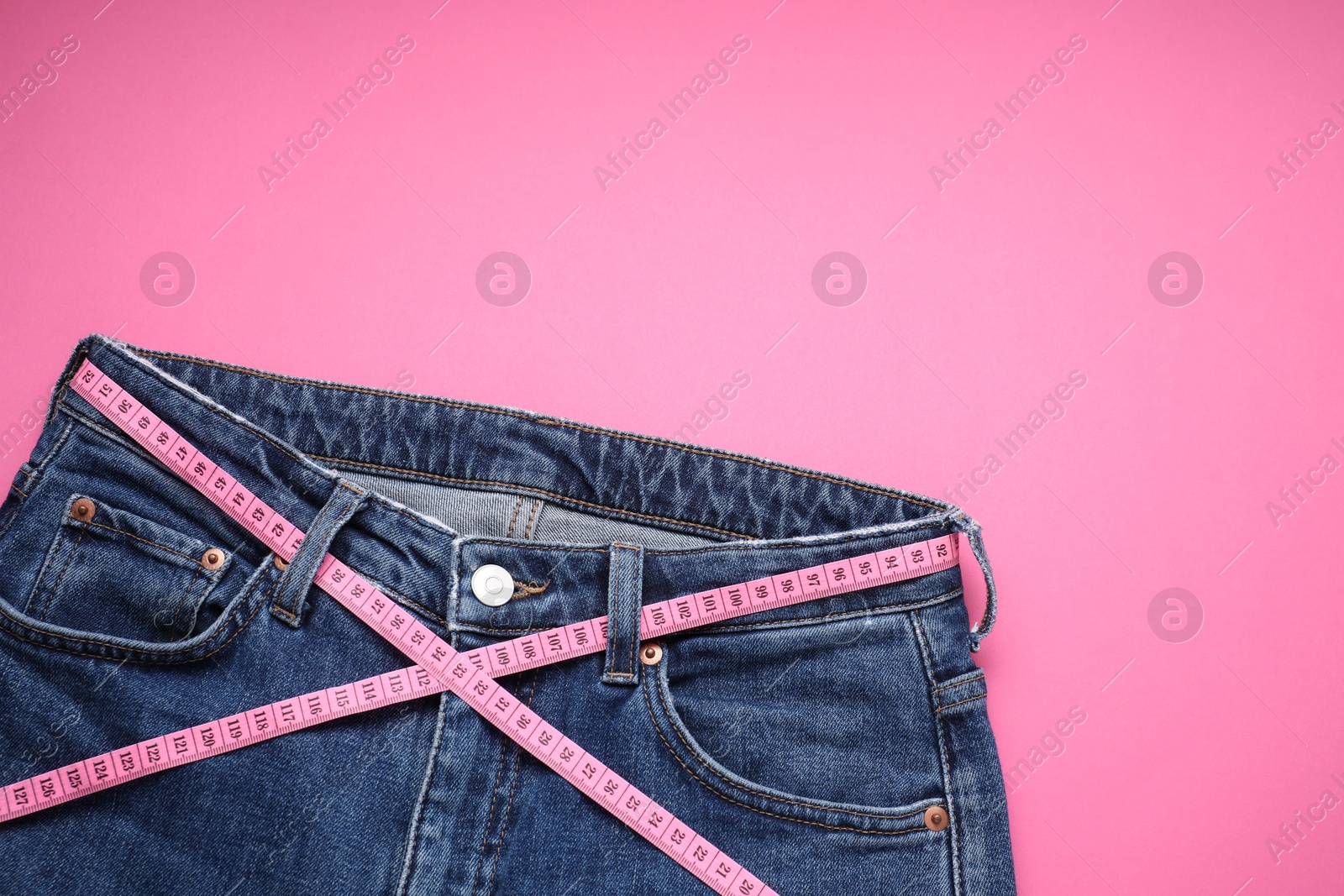 Photo of Jeans and measuring tape on pink background, top view. Space for text