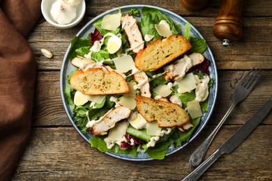 Photo of Tasty Caesar salad with chicken served on wooden table, flat lay