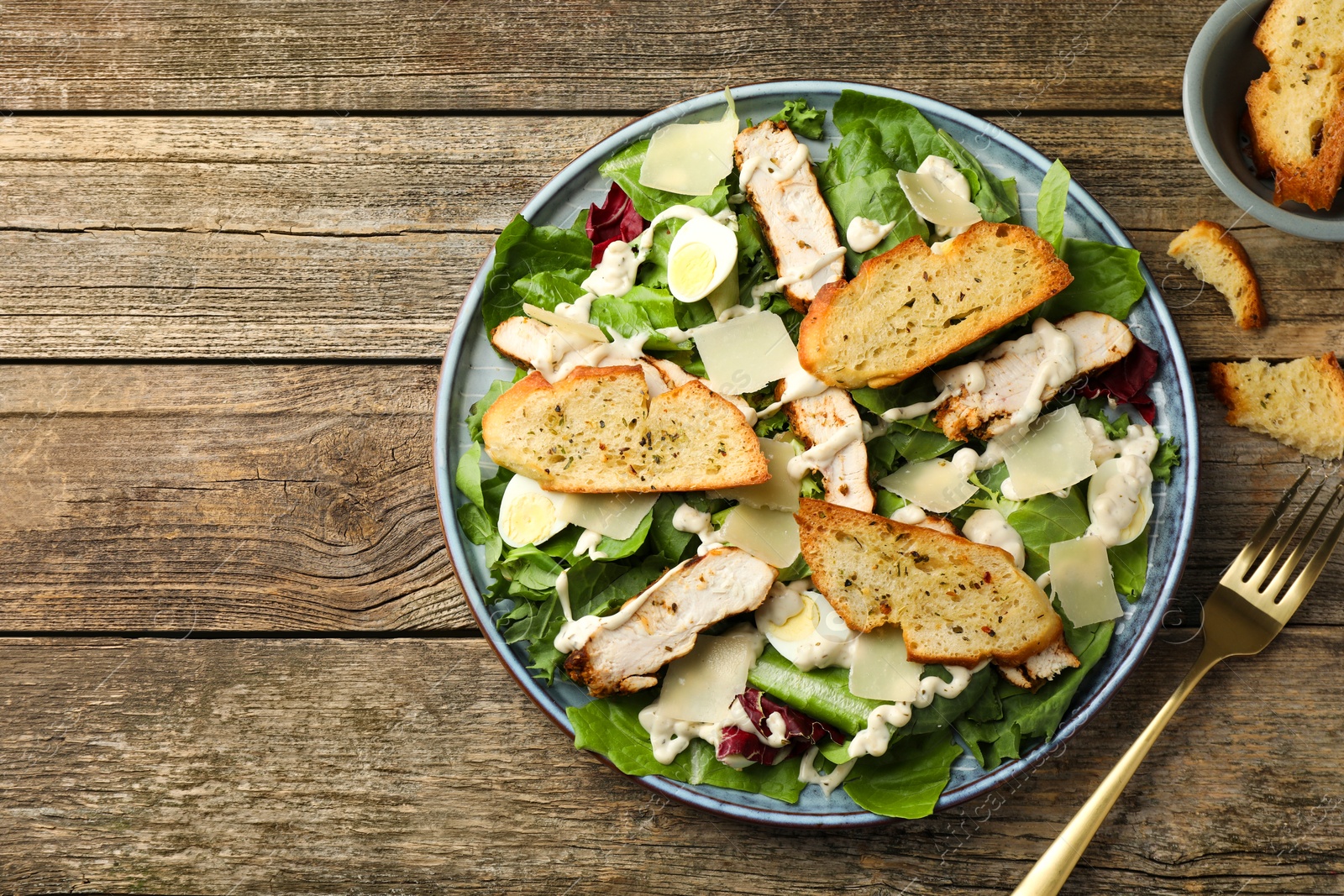 Photo of Tasty Caesar salad with chicken served on wooden table, flat lay. Space for text