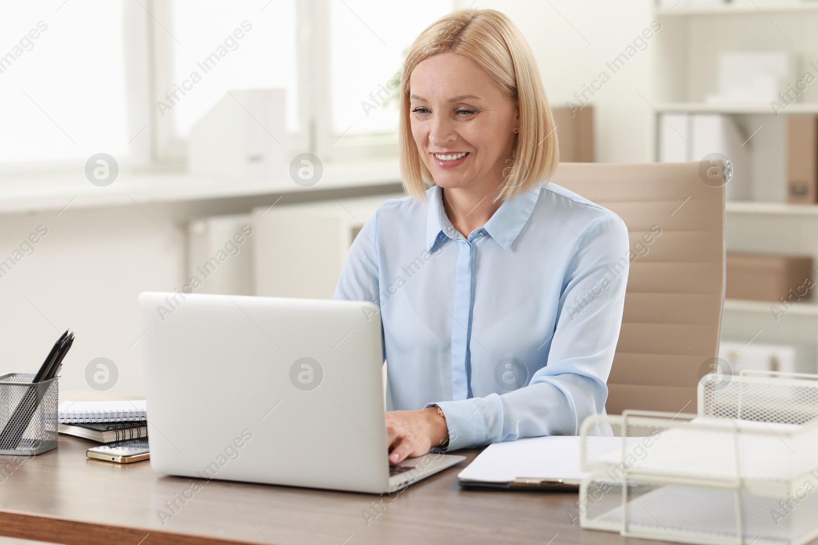 Photo of Smiling middle aged woman working with laptop at table in office