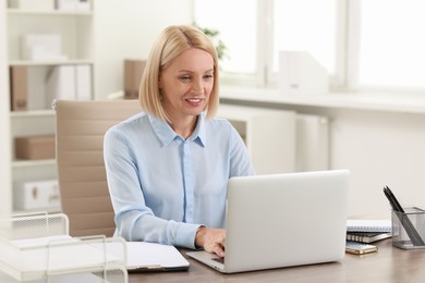 Photo of Smiling middle aged woman working with laptop at table in office